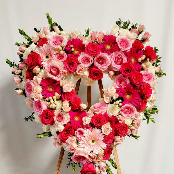 Heart-shaped floral wreath of pink and red roses with gerbera daisies on an easel
