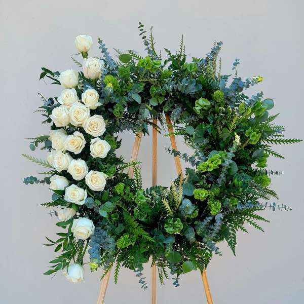 Circular floral wreath of white roses and mixed greenery on a wooden easel