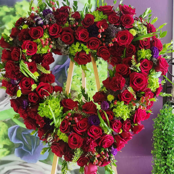 Heart-shaped floral wreath of red roses with green accents on an easel