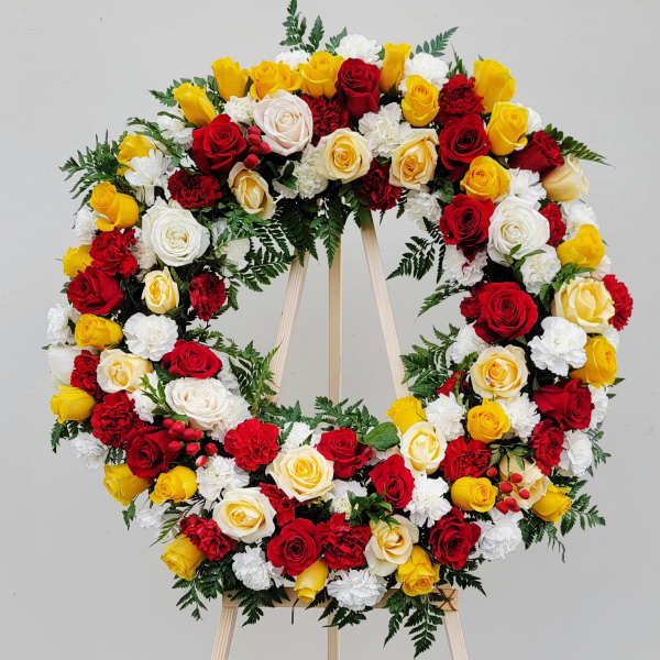 Circular wreath of red, yellow, and white roses on a wooden easel