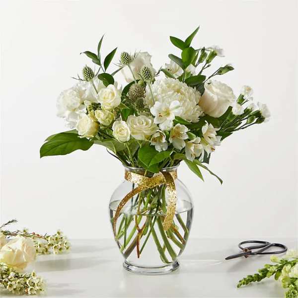 White floral bouquet in a clear glass vase with a gold ribbon