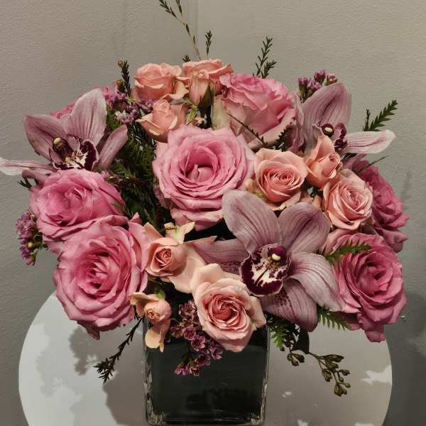 Pink roses and orchids arranged in a square glass vase