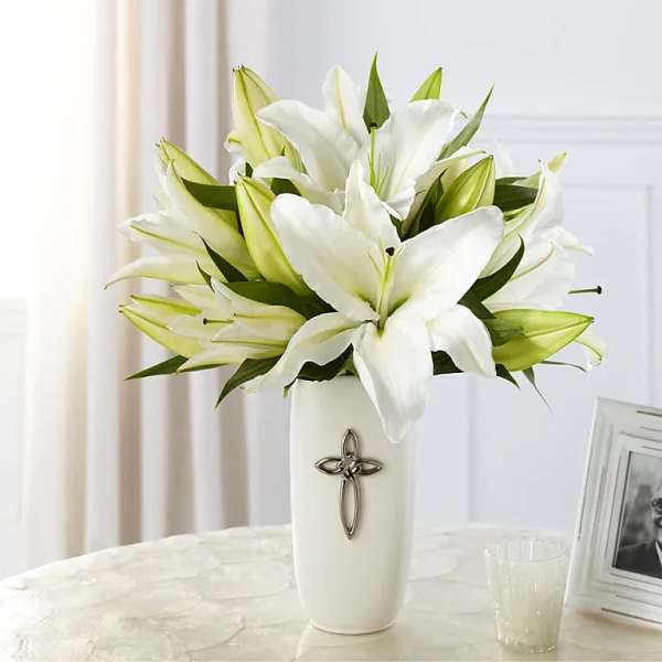 White lilies arranged in a tall white vase with a cross emblem
