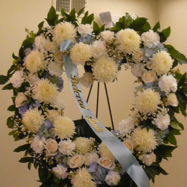 Heart-shaped funeral wreath with white flowers and a blue ribbon on an easel