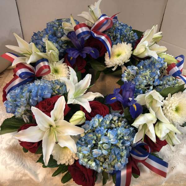 Wreath of blue hydrangeas, white lilies, red roses, and ribbon bows