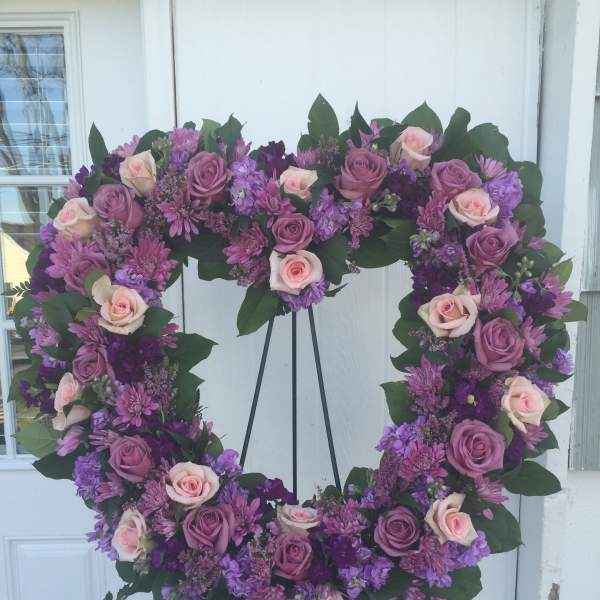 Heart-shaped floral wreath with pink and purple roses on a stand