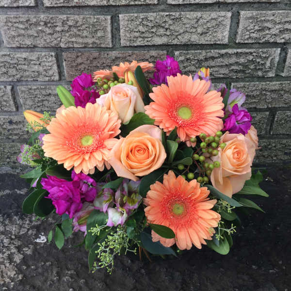 Peach gerbera daisies and roses with purple accents in a low bouquet