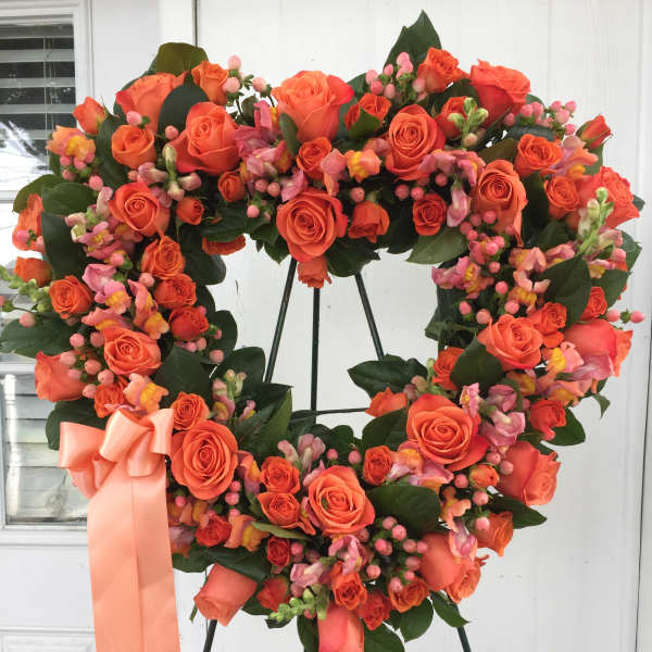 Heart-shaped wreath of orange roses with a peach ribbon on a stand