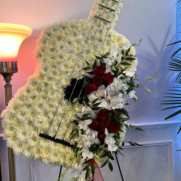 Guitar-shaped floral tribute with white flowers and red roses on an easel