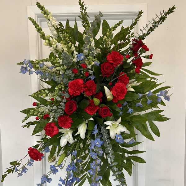 Standing floral spray with red roses, red carnations, white lilies, and blue flowers