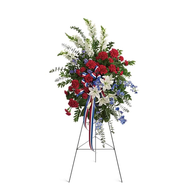 Standing floral spray with red carnations, white lilies, and blue flowers on an easel