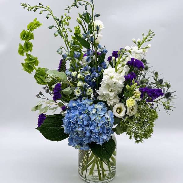 Blue hydrangeas and white flowers in a clear glass vase