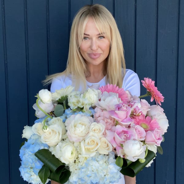 Woman holding a large hatbox arrangement of pink, white, and blue flowers