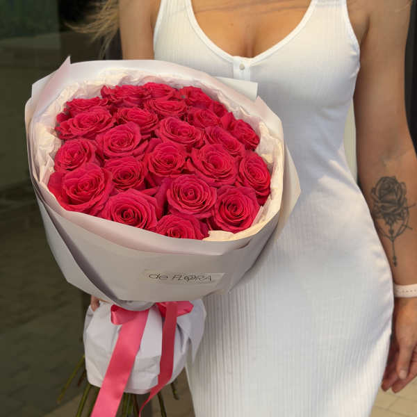 Bouquet of bright pink roses wrapped in pale paper with a ribbon