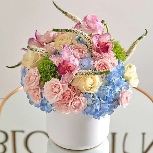 Pastel floral arrangement in a white cylindrical vase with roses and hydrangeas