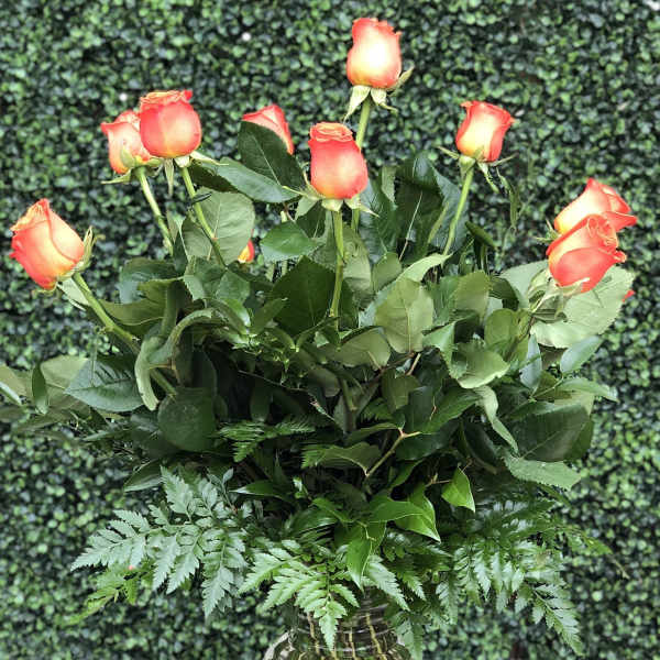 Orange roses arranged in a clear glass vase with fern foliage