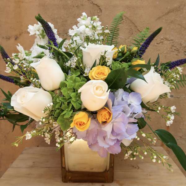 Bouquet of white roses, yellow roses, and purple flowers in a square vase