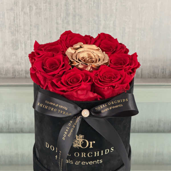Red roses and a gold rose in a black hatbox with a ribbon