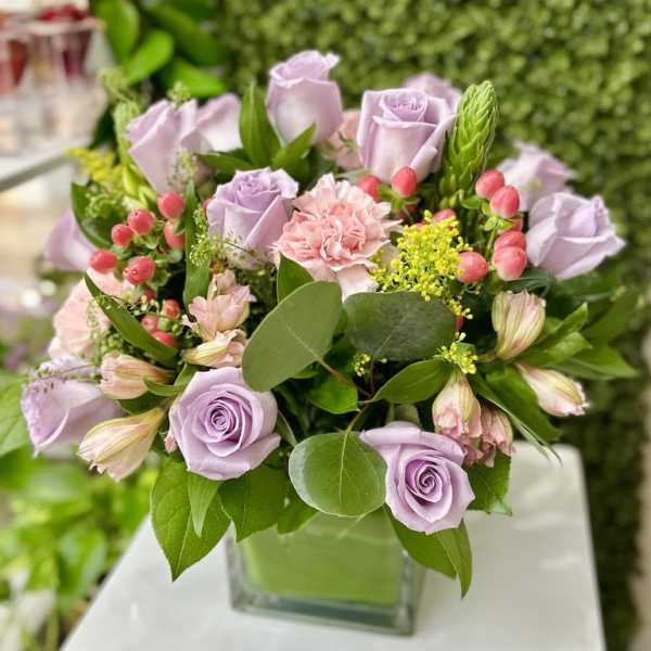 Lavender roses and pink carnations with berries in a square glass vase