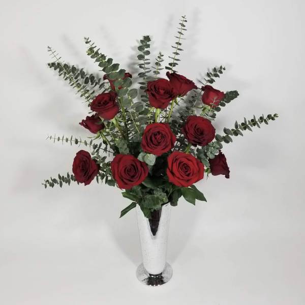 Red roses arranged in a tall white vase with eucalyptus