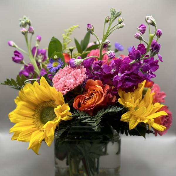 Colorful bouquet with sunflowers, roses, and purple blooms in a glass vase