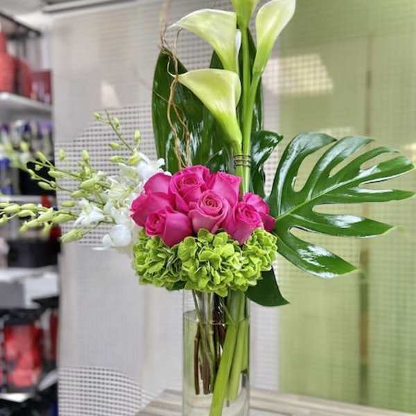 Tall arrangement of white calla lilies, pink roses, green hydrangea and orchids in a clear glass vase
