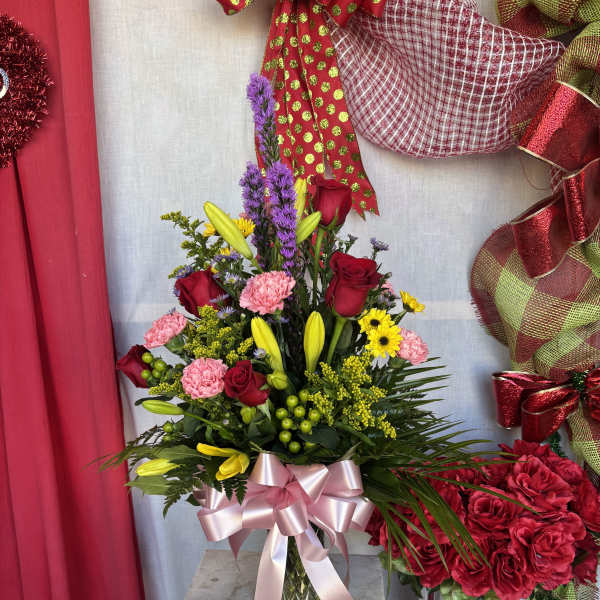 Mixed bouquet of red roses, pink carnations, and yellow lilies in a glass vase