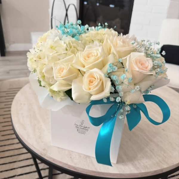 Cream roses and white flowers in a white gift box with a blue ribbon