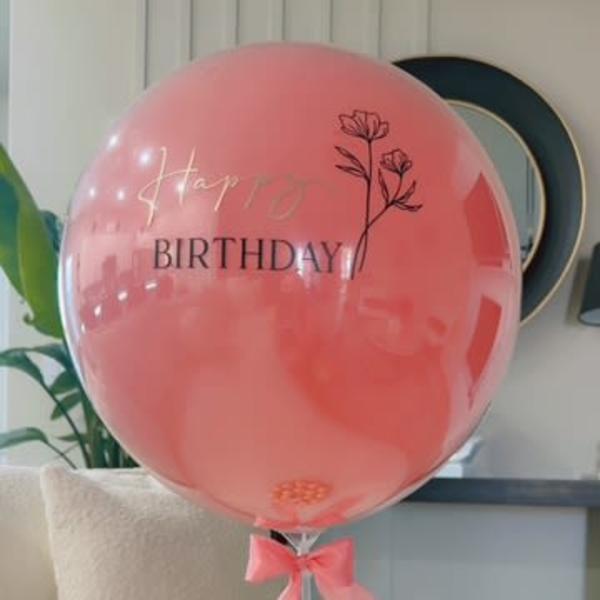 Pink birthday balloon with a ribbon and chocolates below