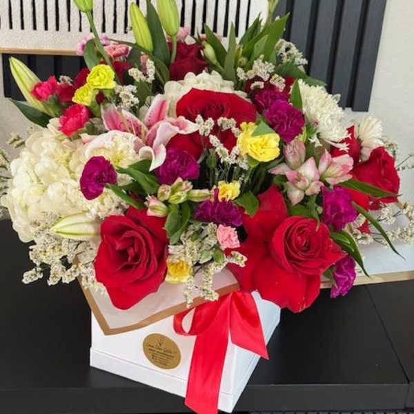 Mixed bouquet of red roses, lilies, and pink flowers in a white box with a red ribbon