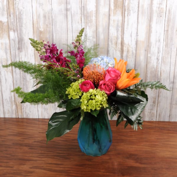 Bright mixed arrangement with pink roses, orange lilies, and green hydrangea in a blue glass vase