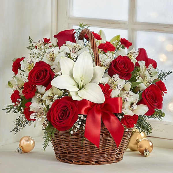 Basket arrangement of red roses, white lilies, and red carnations with a red ribbon