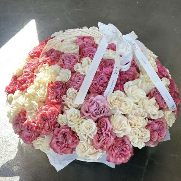 Round basket filled with pink and cream roses tied with white ribbons
