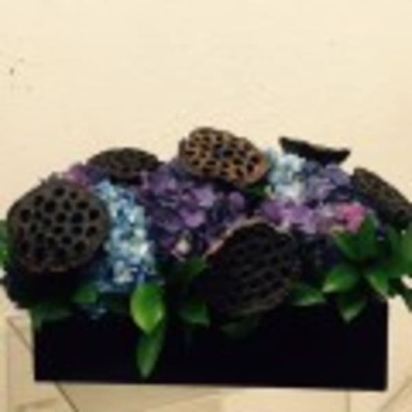 Dark floral arrangement with purple and blue blooms in a black container