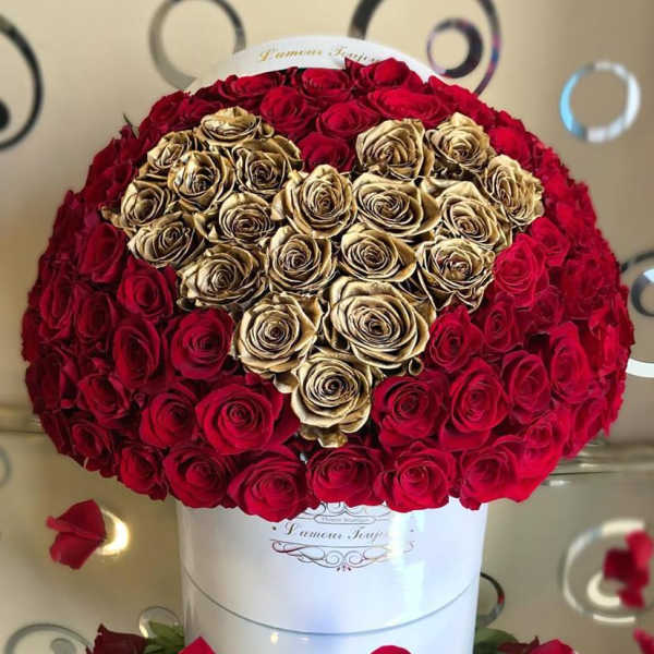 Round box arrangement of red roses with a heart of gold roses on a reflective surface
