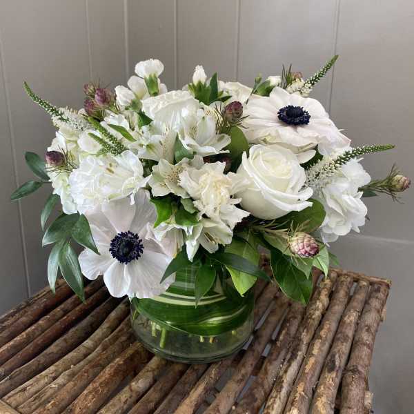 White floral arrangement in a glass vase with dark-centered blooms
