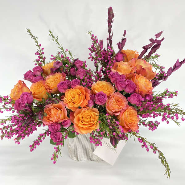 Orange and magenta roses in a white vase with purple filler flowers