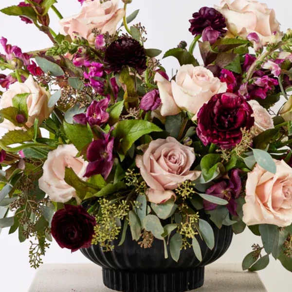 Bouquet of pale pink roses and deep burgundy flowers in a black vase