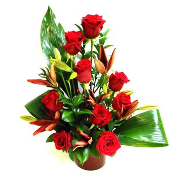 Red roses and lilies arranged with large green leaves in a low round container
