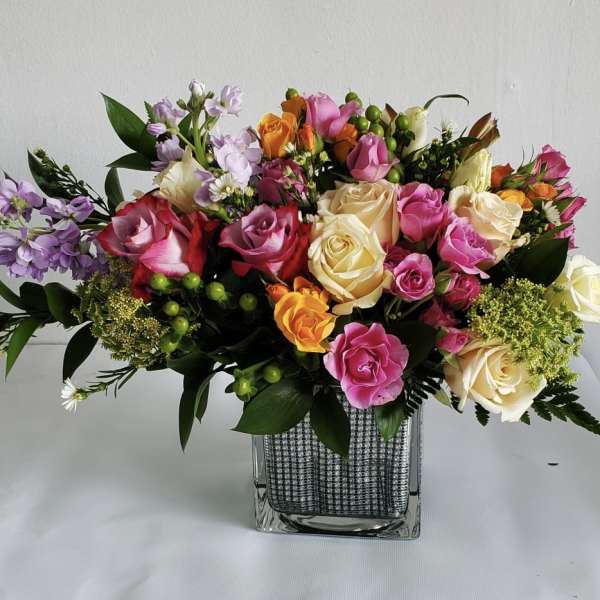 Mixed bouquet of pink, cream, and orange roses with accent flowers in a square glass vase