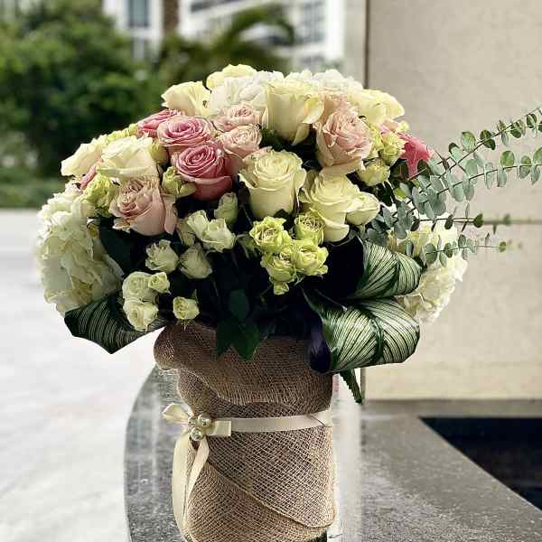 Bouquet of pink and cream roses in a burlap-wrapped vase