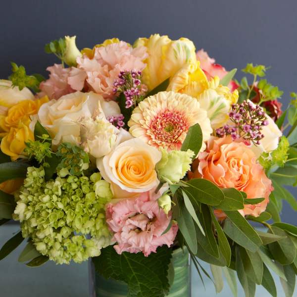 Mixed bouquet of pastel roses, carnations, and gerbera daisies in a glass vase