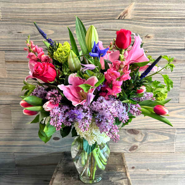 Mixed bouquet of pink, purple, and red flowers in a clear glass vase