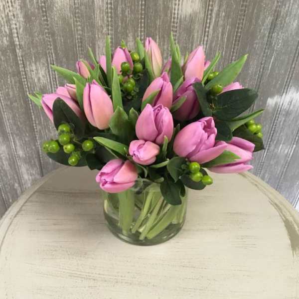 Pink tulips arranged in a clear glass vase with green berries