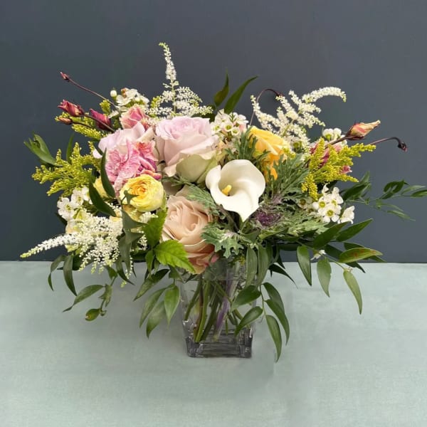 Mixed bouquet of pastel roses, calla lily, and white filler flowers in a glass vase