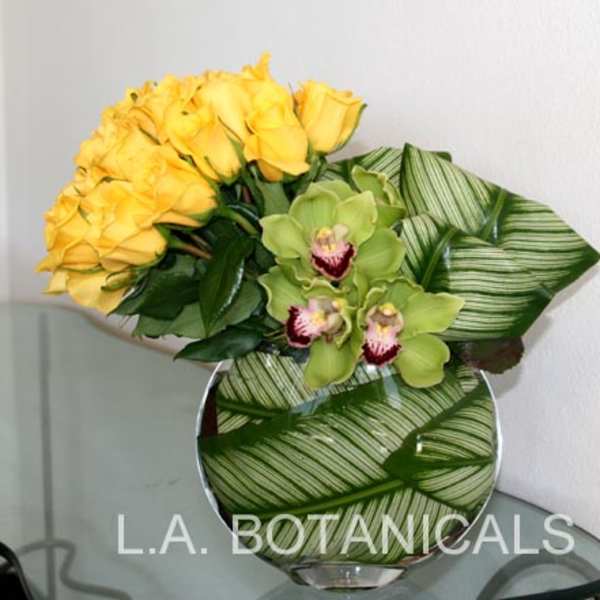 Yellow roses and green orchids in a round glass vase