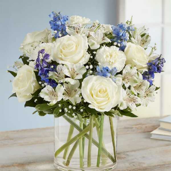 White roses and blue flowers arranged in a clear glass vase