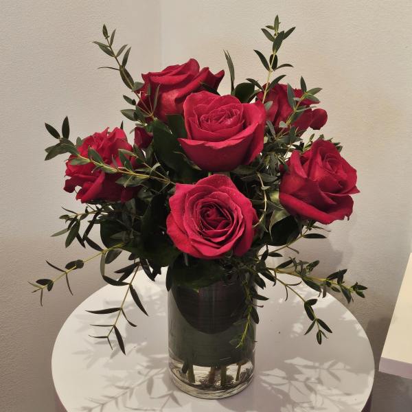 Red roses arranged in a clear glass vase with dark greenery