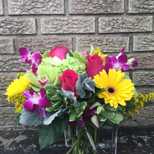 Bright mixed bouquet with yellow daisies, pink roses, and purple orchids in a glass vase