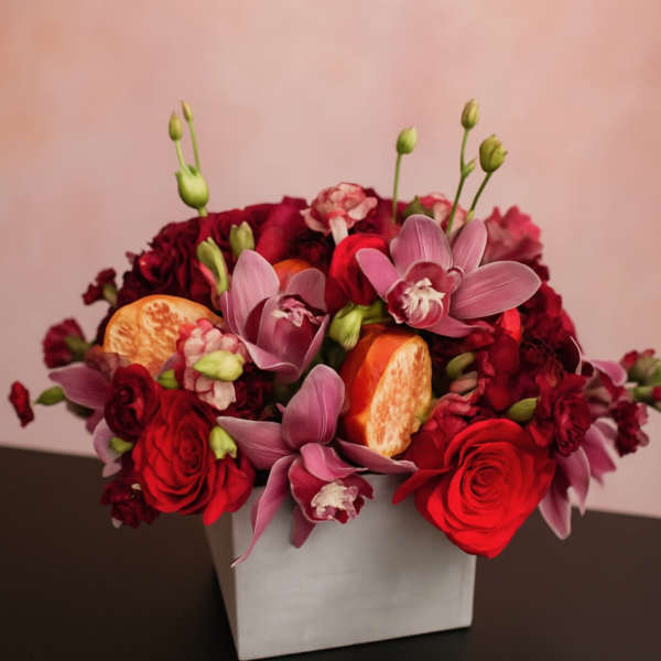 Red and pink floral arrangement in a white square vase